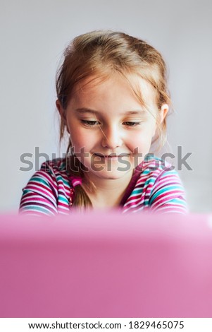 Little girl preschooler learning online solving puzzles playing educational games listening to sounds watching video on tablet during COVID-19 quarantine sitting at desk in front of computer