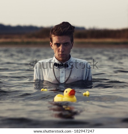 Artistic portrait of hipster style young man with yellow ducks in water Royalty-Free Stock Photo #182947247