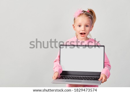 Closeup portrait of cute girl 4-5 year old in pink showing laptop screen with mock up on gray background