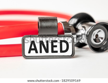 ANED Alive no evidence of disease lettering on a business card with a holder, next to the red stethoscope. Medical concept. Treatment and prevention. Human health.