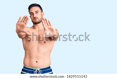 Young handsome man wearing swimwear doing frame using hands palms and fingers, camera perspective 
