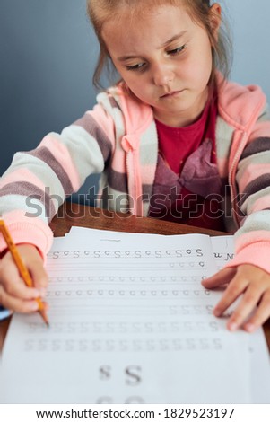 Little girl preschooler learning to write letters reluctantly. Kid writing letters, doing a school work unwillingly. Concept of early education