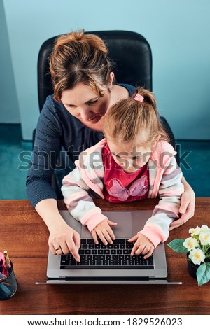 Little girl preschooler learning online solving puzzles playing educational games typing letters listetning to music and sounds with help of her mother using laptop computer and sitting at desk