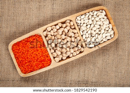 White beans, dried chickpeas and red lentils on a wooden plate.
