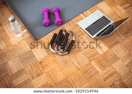 Detail from a living room of a modern house with yoga mat, laptop, water and purple dumbbells. Fitness at home, laptop for online video training