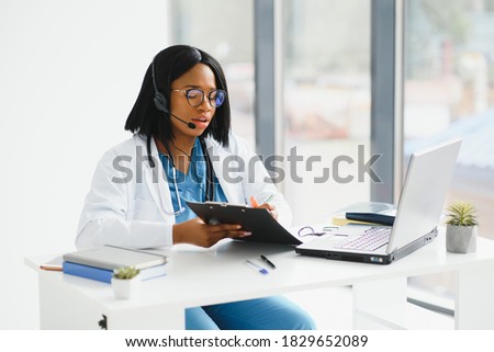 African doctor wear headset consult patient make online webcam video call on laptop screen. Telemedicine videoconference remote computer app virtual meeting. Over shoulder videocall view. Royalty-Free Stock Photo #1829652089