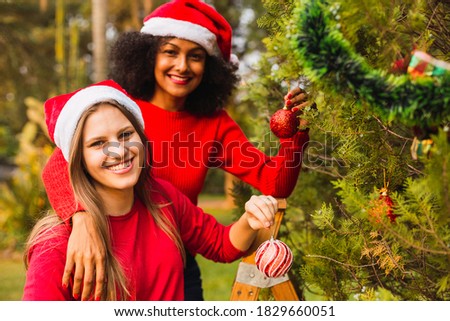 Young friends at the Christmas tree. Multiracial friends in the park. Friends decorating the Christmas tree. Concept of Christmas and friendship.