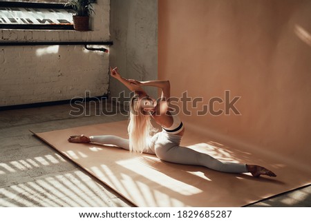 Atmospheric and dark studio room and alone graceful and attractive female athlete posing landing in a split with raised hands in it.