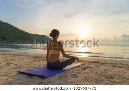 Woman sitting in lotus position and meditating at sunrise on the beach
