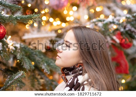 Christmas theme. Young beautiful European girl on a background of a Christmas tree, lights and toys in a joyful mood, happy, dreams of gifts.