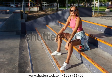 Funny stylish young woman skater with cruiser board sits on the stairs in the skatepark