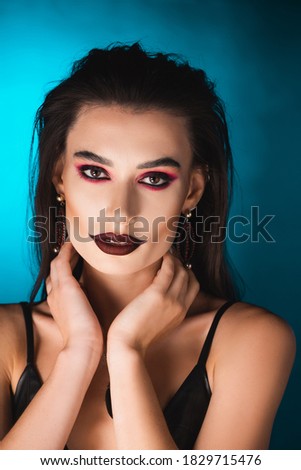 young woman with dark makeup looking at camera on blue