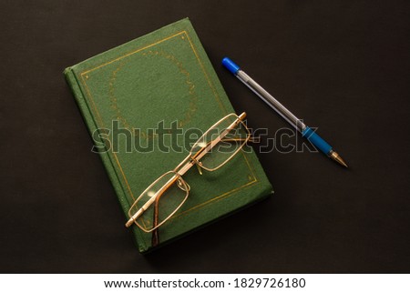 Reading glasses on a closed book with blue pen on a black background. Top view. Copy space. Education and self-education, development during quarantine