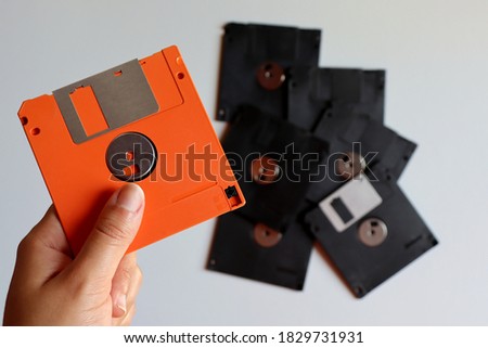 Woman's hand holding floppy disk (diskette). Orange Floppy Disk. Obsolete technology.