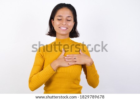 Young woman with short hair wearing casual yellow sweater isolated over white background smiling with hands on chest with closed eyes and grateful gesture on face. Health concept.