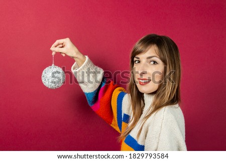Smiling young woman holding in hand a decorative silver ball on a burgundy background. Concept preparation for the holidays, Rozhdestovo, New Year