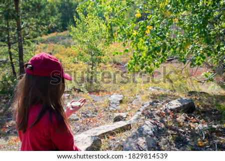 A girl in a red sports cap looks at a compass in her hand on a Sunny day in the woods.The view from the back . The concept of search road