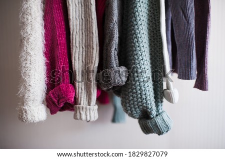 Knitted clothes with folded sleeves hang on hanger indoors closeup. Winter season. 