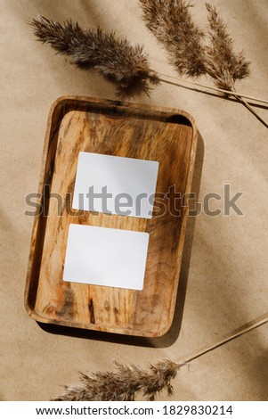 Top view of two blank paper sheet cards on a wooden tray with dry grass. Beige or sand tones. Mockup for business template, copy space.
