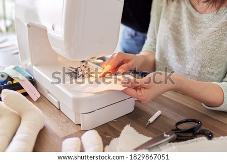 Adult woman sews on a sewing machine sitting at home at table. Hobbies, handmade, profession, skills, creativity, work at home