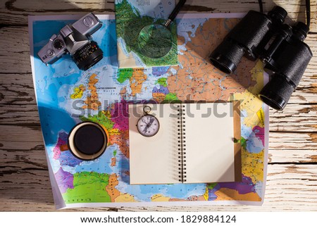 Flat lay of the travel planning concept. Top view of a diary, binoculars, compass, retro photo camera, coffee, and Europe map on a white wooden table