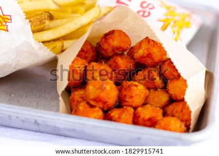 Close up of orange sweet potato tots on a gray tray with French fries in the background