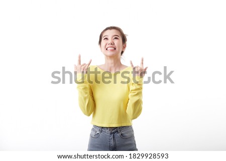 Positive joyful Young asian woman with short hair makes heavy metal sign wearing wearing a mustard pullover People and emotions concept