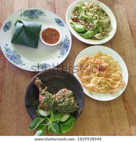 A complete set for lunch consisting of rice wrapped in banana leaves, green peppered penyet chicken, sambal belacan, omelet and salted fish kailan vegetables. Menu in asian restaurant concept.