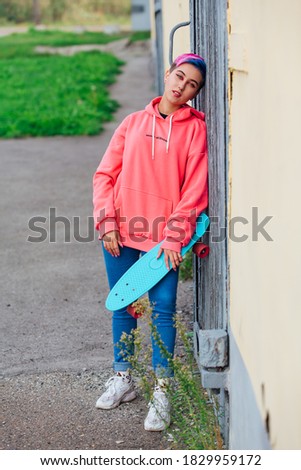 Stylish young woman with short colored hair holding blue plastic skateboard in hand. Youth concept.