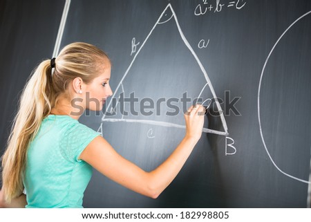 Pretty young elementary school/college teacher writing on the chalkboard/blackboa rd during a math class (color toned image; shallow DOF)