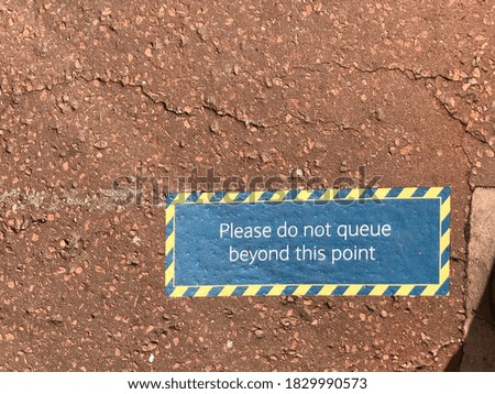 A street sign on floor indicates where to stand to maintain social distancing . ‘Please do not queue beyond this point’.