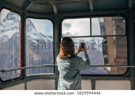 Young traveler taking photo of mountains on her smartphone through sky lift window. Student girl spending her holidays in nordic country.