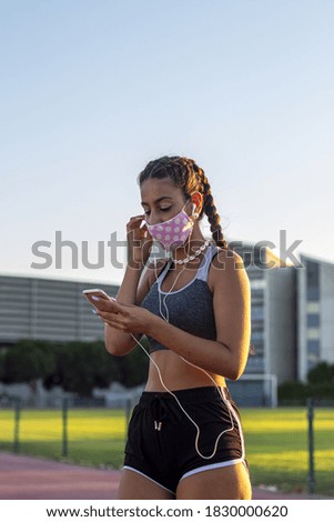 A selective focus shot of a young female with a mask listening to music in the park