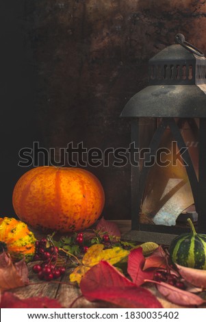 a dark autumn background, on raw wood colorful leaves and a pumpkin, next to them an old lantern with a broken glass