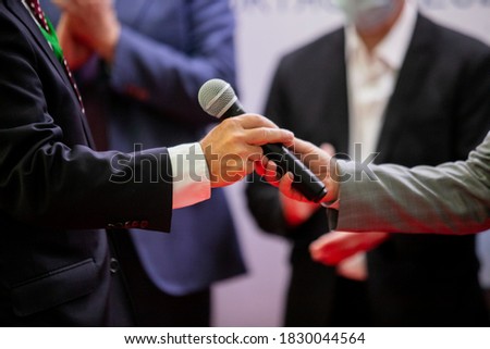 The presenter hands over the microphone to an important person for a solemn speech