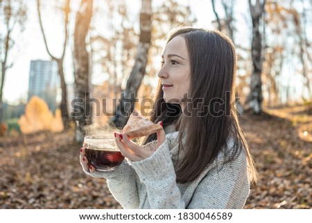 A young pretty woman is eating pizza and drinking hot tea in an autumn yellow Park in the sunset light. The concept of a cozy lifestyle in the autumn cold season