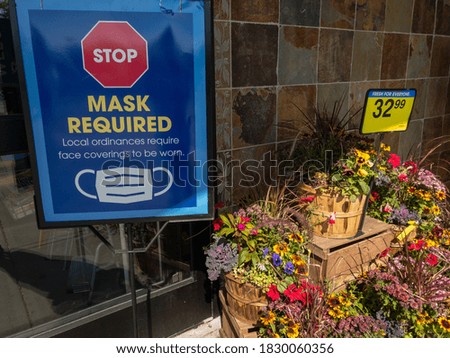Store face mask required sign next to fall flowers for sale.