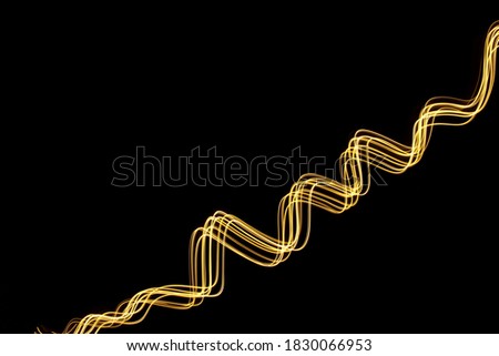 Long exposure photograph of neon gold colour in an abstract swirl, parallel lines pattern against a black background. Light painting photography.