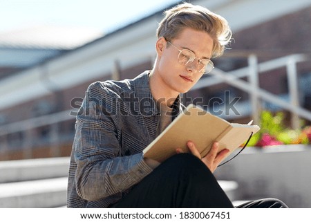 leisure, education and people concept - young man or teenage boy in glasses with notebook, diary or sketchbook writing or drawing in city Royalty-Free Stock Photo #1830067451