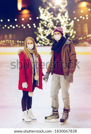 holidays and leisure concept - couple wearing face protective medical masks for protection from virus disease holding hands at outdoor skating rink over christmas tree background