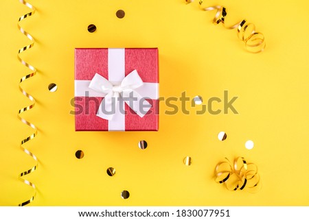 Red gift box on yellow background with golden confetti and rolls.