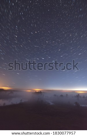Star trails around North Star over misty bog landscape and city lights on the horizon