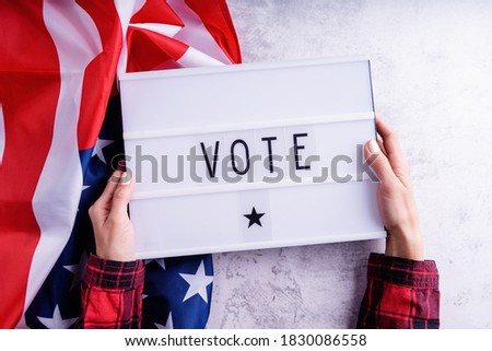 Top view of woman hands holding lightbox with the word Vote on american flag background