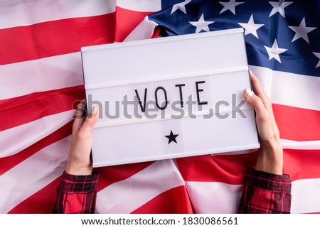 Top view of woman hands holding lightbox with the word Vote on american flag background