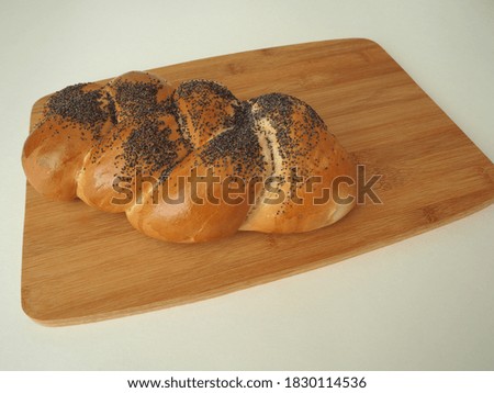 Fresh bread on a wooden tray. A cosy bun with a close-up poppy.