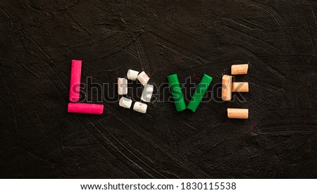 Multi-colored pastel crayons on a black background. The word Love is made of crayons. A symbol of love and unity. Extended horizontal banner. Creative layout of a Valentine's day greeting card.
