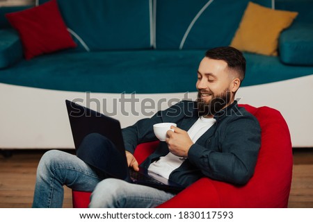 Bearded male freelancer making coffee break while working remotely on laptop computer in home office.
