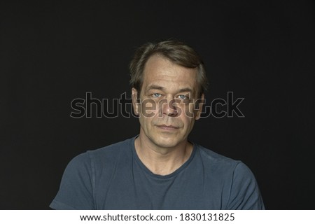 Portrait of a man in a Studio 40-50 years old in a blue t-shirt on a black blurry background, close-up. Maybe he's just a buyer, an actor or a truck driver, a loader or a military pensioner