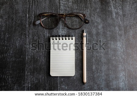 Modern staionery scene. open notebook pencil and stylish glasses on black wooden background. flat lay top view