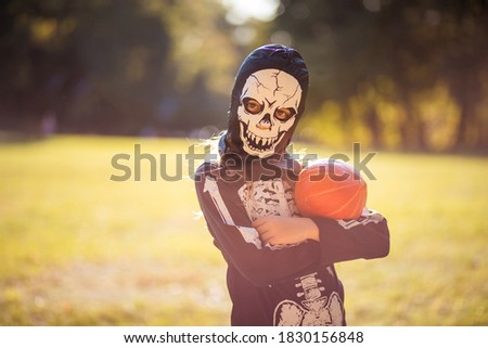 She is scary for Halloween.  Little girl in skeleton suit standing in nature and holding pumpkin. 